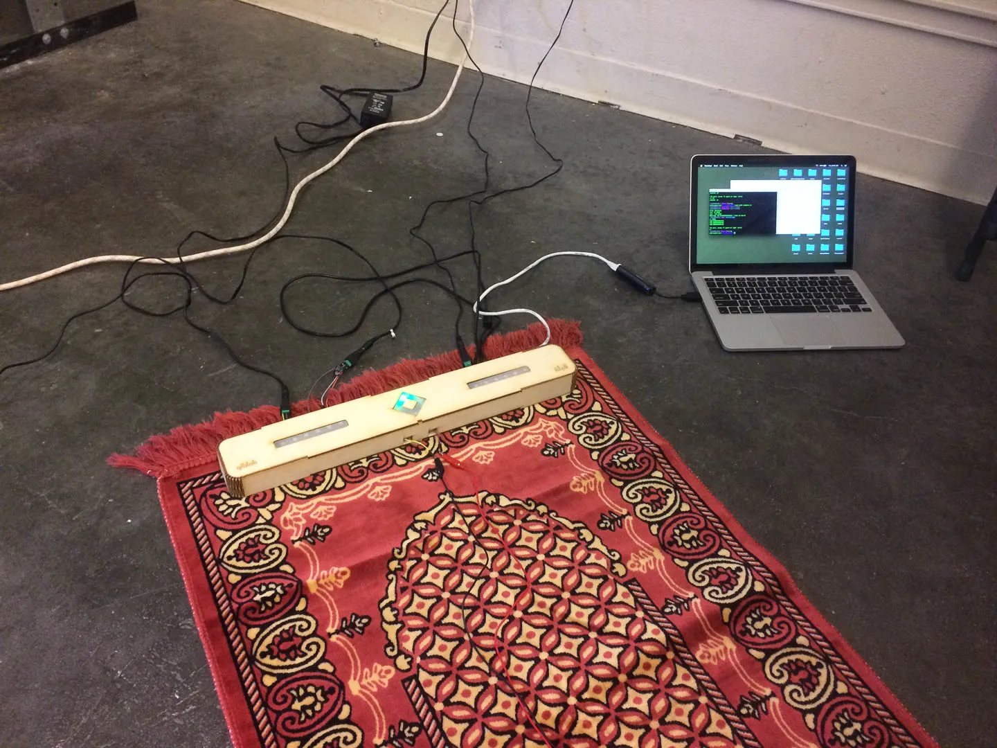 Early prototype on prayer rug. The device sits at the foot of the rug, oriented by the compass toward the Ka'aba.